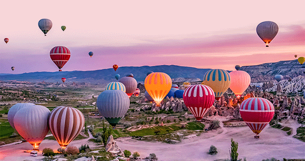Numerose mongolfiere colorate fluttuano su un paesaggio di valle rocciosa durante un'alba rosa e viola.
