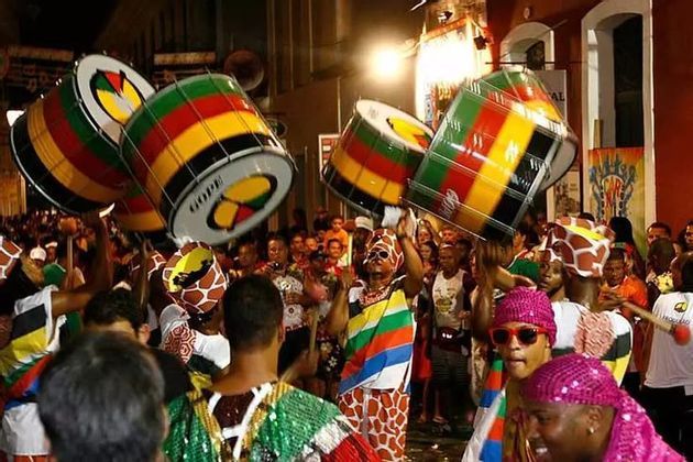 Une foule de personnes en costumes colorés célèbrent lors d'un défilé de rue la nuit, jouant de grands tambours rayés.