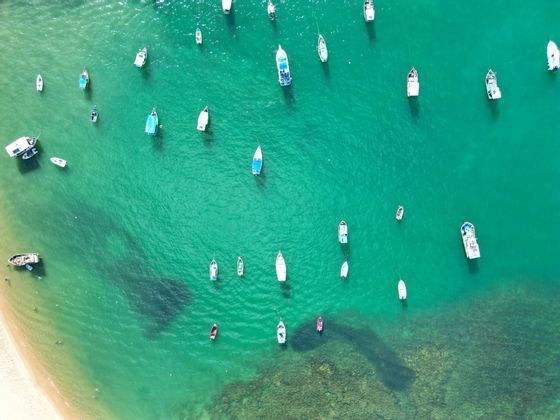 Une vue aérienne de petits bateaux flottant dans l'eau turquoise peu profonde près d'une plage de sable.
