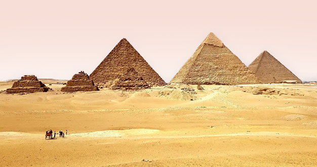 Eine Weitaufnahme von mehreren Pyramiden unterschiedlicher Größe, die in einer weiten Sandwüste unter einem dunstigen Himmel stehen.