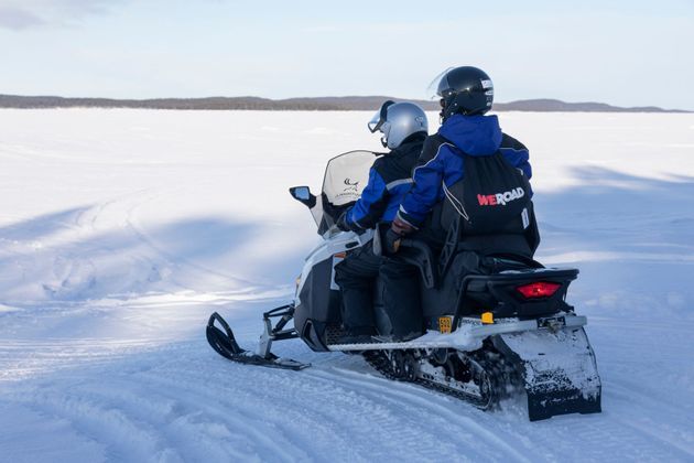 Zwei Personen einer WeRoad Gruppenreise fahren mit einem Schneemobil durch eine weite, sonnige, schneebedeckte Landschaft.