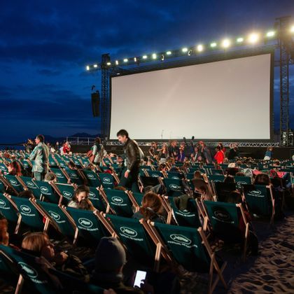 Une foule se rassemble sur des transats sur une plage pour une projection en plein air au Festival de Cannes la nuit.