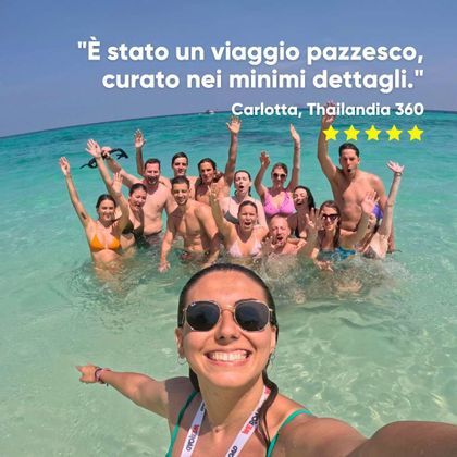 Una donna si scatta un selfie con il suo gruppo di viaggio WeRoad, tutti sorridenti e che salutano, immersi in acqua turchese cristallina.