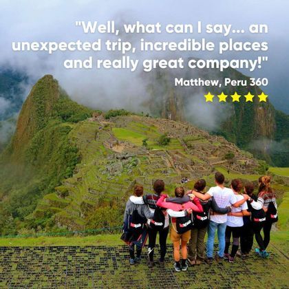 A WeRoad group trip stands with arms around each other, looking out at ancient ruins on a green, misty mountainside.