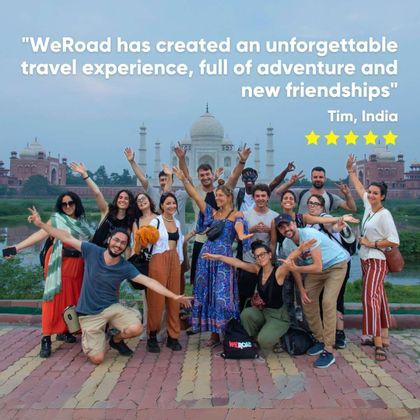 A WeRoad group trip of people smiling and posing for a group photo in front of the Taj Mahal at dusk.