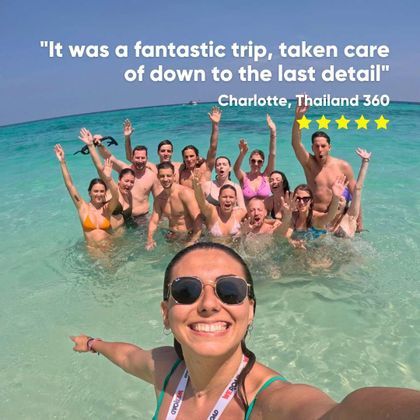 A woman takes a smiling selfie with her WeRoad group trip as they wave from the clear, turquoise water.