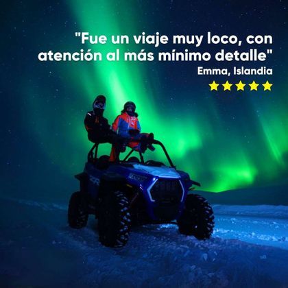 Dos personas de un viaje en grupo de WeRoad están sentadas en un vehículo todoterreno azul en un paisaje nevado bajo la aurora boreal.
