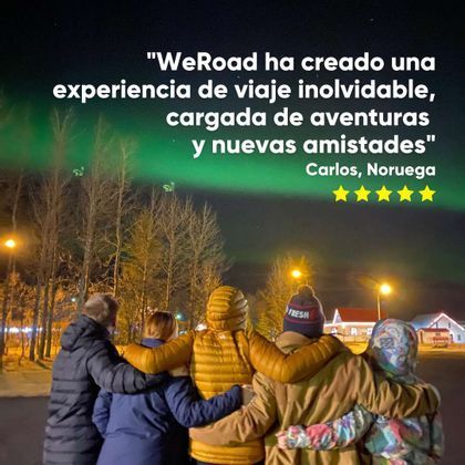 Un grupo de WeRoad de cuatro personas, con los brazos entrelazados, contempla la aurora boreal verde en el cielo nocturno.