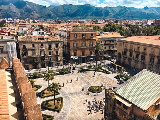 Veduta aerea di un viaggio di gruppo WeRoad in una piazza di città, circondata da edifici storici e con una catena montuosa sullo sfondo.