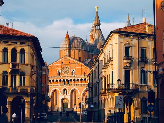 Una gran basílica con múltiples cúpulas y agujas al final de una calle con edificios amarillos al atardecer.
