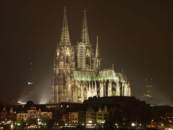 Eine beleuchtete gotische Kathedrale mit zwei großen Türmen beherrscht die Skyline einer Stadt bei Nacht.