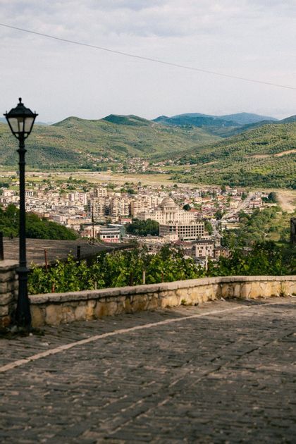 Une vue depuis une rue pavée surplombant une ville nichée dans une vallée, avec un lampadaire au premier plan et des collines verdoyantes à l'arrière-plan.