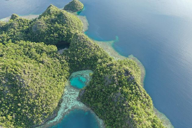 Vista aérea de exuberantes islas verdes y montañosas, rodeadas de un océano azul profundo y lagunas turquesas poco profundas con arrecifes de coral visibles.