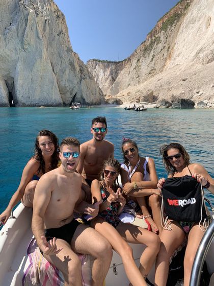 Un viaggio di gruppo WeRoad con persone sorridenti in posa su una barca in mare con alte scogliere bianche sullo sfondo.