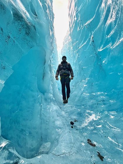 Un homme équipé pour l'hiver et muni de crampons traverse un passage étroit à l'intérieur d'une grotte de glace bleu vif.