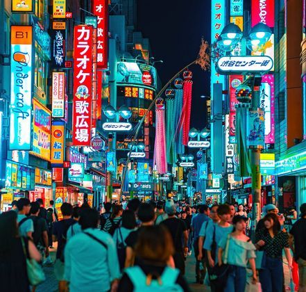 Una multitud de personas camina por una concurrida calle japonesa de noche, iluminada por altos edificios cubiertos de coloridos letreros de neón.