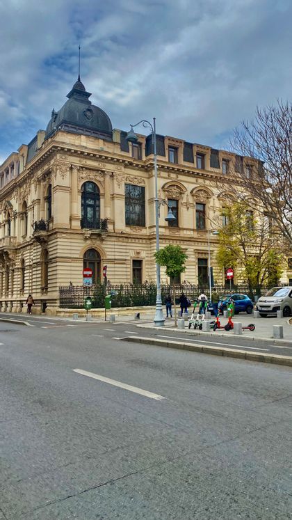 Un edificio ornamentado de estilo clásico con un techo abovedado oscuro en la esquina de una calle de la ciudad bajo un cielo nublado.