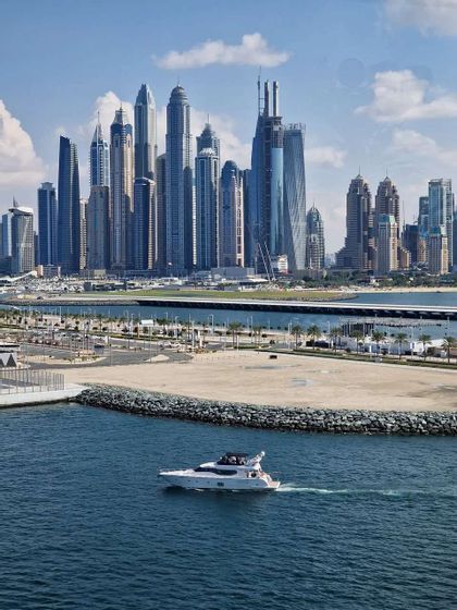 A white motor yacht cruises on blue water with a modern skyline of numerous tall skyscrapers in the background.