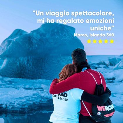 Un uomo e un capogruppo WeRoad si abbracciano da dietro mentre guardano un grande iceberg blu in un paesaggio innevato.
