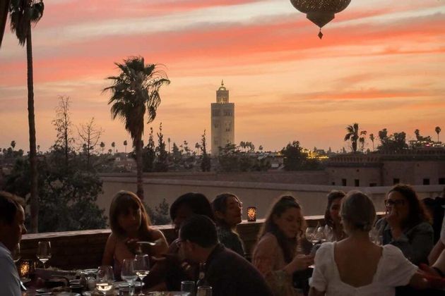 Cena di gruppo WeRoad su terrazza panoramica al tramonto, con vista su skyline e minareto.
