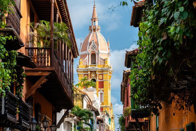Un clocher d'église coloré avec un dôme rose se dresse au bout d'une rue bordée de bâtiments coloniaux aux balcons en bois.