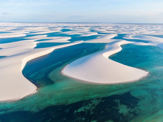 Una veduta aerea di vaste dune di sabbia bianca, separate da lagune tortuose di acqua turchese e blu, sotto un cielo limpido.