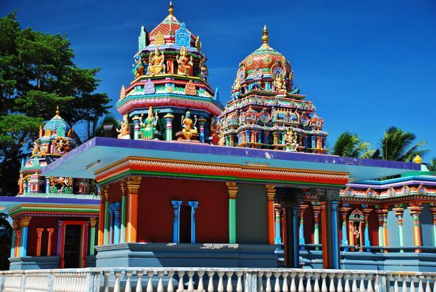 Un temple hindou aux couleurs vives, avec des tours finement sculptées et ornées de statues, se détachant sur un ciel bleu clair.