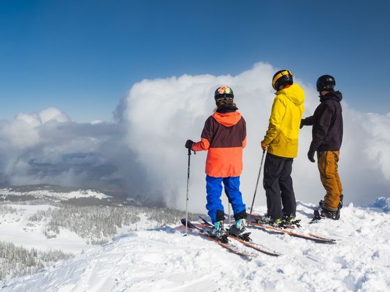Un viaggio di gruppo WeRoad con tre sciatori su una vetta innevata, che ammirano una valle avvolta dalle nuvole.