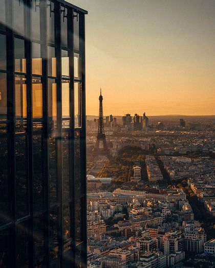 Un extenso paisaje urbano con una torre a la distancia, visto desde un moderno edificio de cristal durante un atardecer dorado.