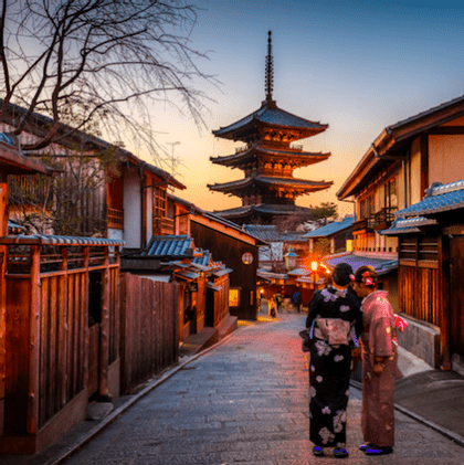 Deux femmes en kimonos traditionnels se tiennent dans une rue historique face à une pagode japonaise au coucher du soleil.