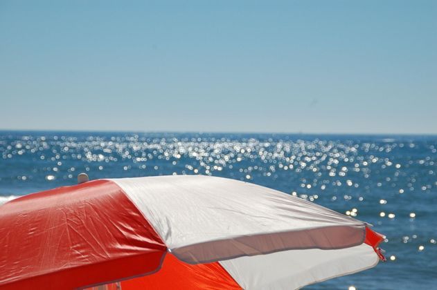 Primo piano di un ombrellone da spiaggia rosso e bianco, con il sole che scintilla sul mare blu sullo sfondo.