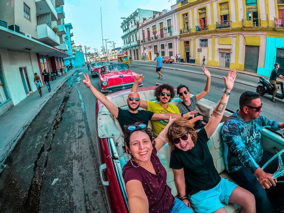 Un grupo de WeRoad sonríe para una selfie mientras pasea en un coche descapotable clásico rojo por una calle de la ciudad.