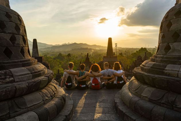 Un gruppo WeRoad è seduto abbracciato, ammirando un paesaggio della giungla da un tempio di pietra al tramonto.