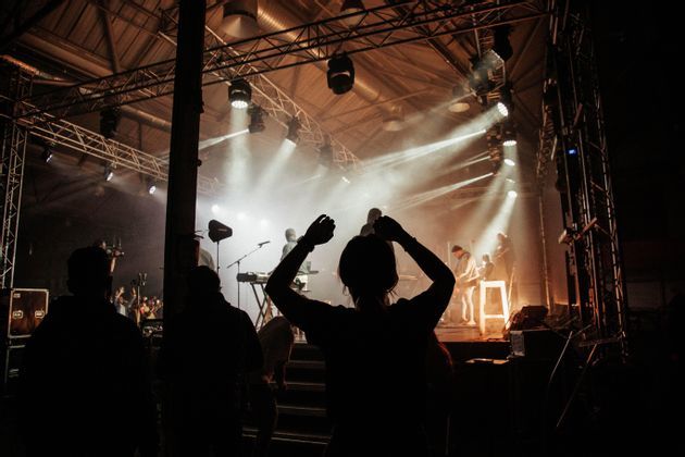 Sagome di un pubblico osservano una band esibirsi su un palco avvolto nel fumo e illuminato da potenti riflettori.