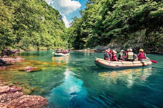 Voyage de groupe WeRoad : rafting en bateaux gonflables sur une rivière turquoise serpentant dans un canyon luxuriant.