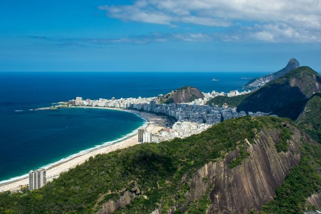Une vue aérienne d'une ville côtière le long d'une plage de sable incurvée, nichée entre des montagnes verdoyantes et l'océan bleu.