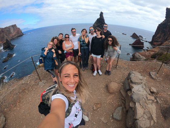 Una donna si fa un selfie con un viaggio di gruppo WeRoad su una scogliera che si affaccia su una costa rocciosa e l'oceano.