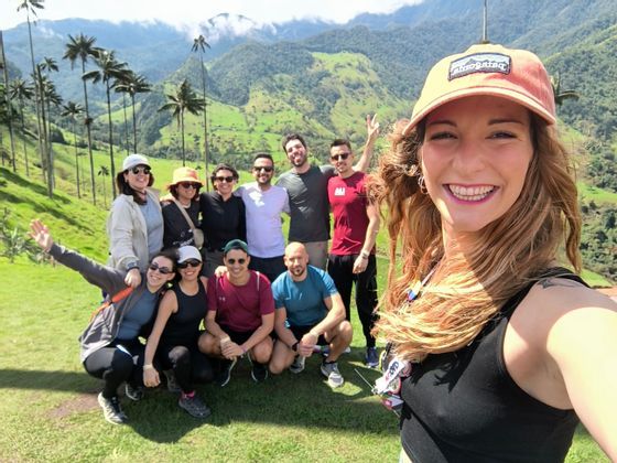 Eine WeRoad-Gruppe posiert für ein Gruppenselfie auf einem grünen Hügel mit hohen Palmen und Bergen im Hintergrund.