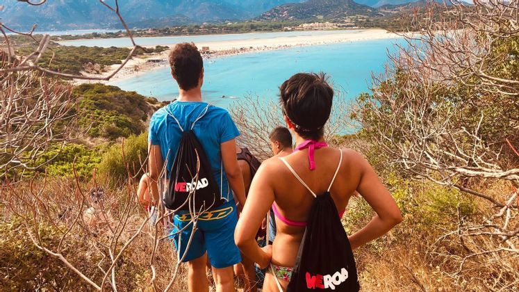 A WeRoad group trip on a hill looking out over a crowded sandbar beach and turquoise water.