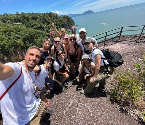 Un viaje en grupo de WeRoad posa para una selfie grupal en un acantilado rocoso con vistas a una costa boscosa y el mar.