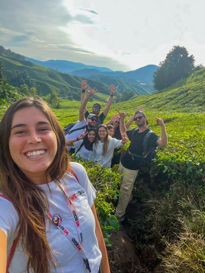 Un groupe WeRoad sourit pour un selfie au milieu d'une vaste plantation de thé, avec des collines verdoyantes en toile de fond.
