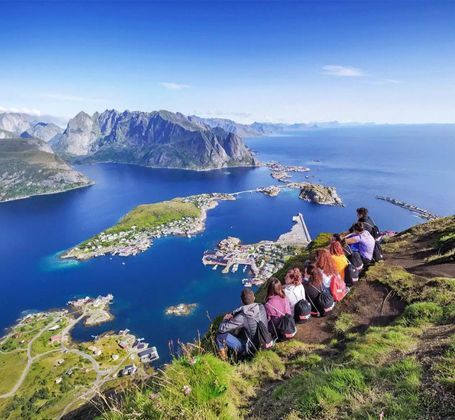 Un viaggio di gruppo WeRoad su una scogliera verdeggiante, che si affaccia su una città costiera e una baia circondata da montagne sotto un cielo sereno.