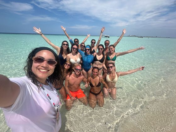 Un gruppo WeRoad in viaggio si scatta un selfie mentre è in piedi in acque basse e limpide color turchese in una giornata di sole.