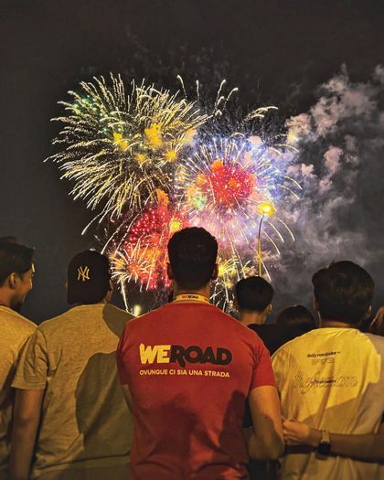 Un viaje en grupo de WeRoad visto desde atrás observando un colorido espectáculo de fuegos artificiales contra el oscuro cielo nocturno.