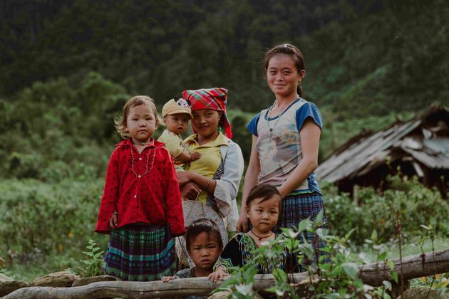 Una mujer y cinco niños con ropa colorida posan para una foto en un paisaje rural exuberante y verde.