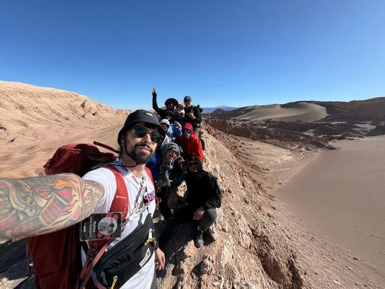 Un gruppo WeRoad si fa un selfie su un crinale roccioso che domina un vasto paesaggio desertico sotto un cielo azzurro.