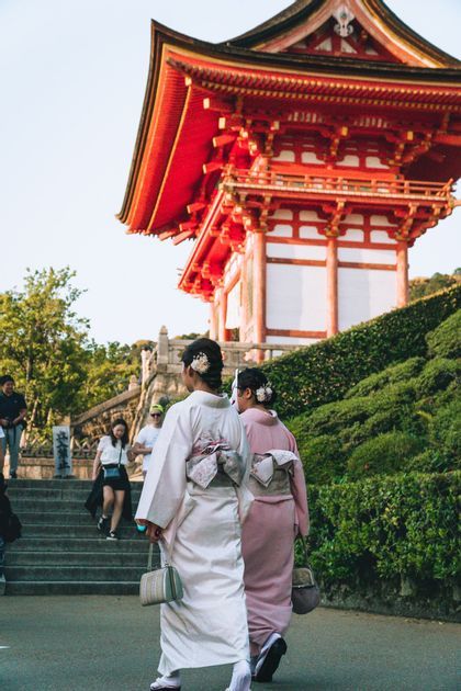 Due donne viste di spalle in kimono tradizionale camminano su un sentiero verso una pagoda giapponese rossa su una collina