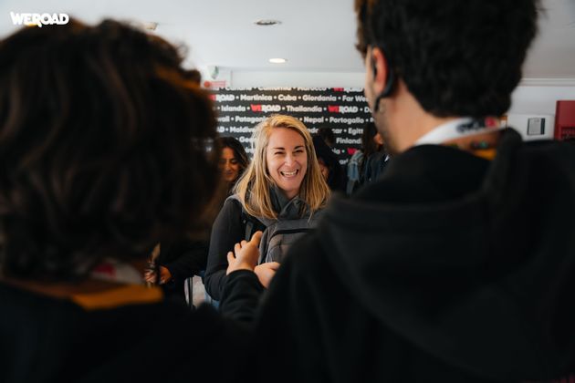 A blonde woman laughs while talking with two other people during a WeRoad group trip gathering.