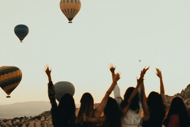 Silhouettes d'un groupe WeRoad les bras levés, observant des montgolfières flotter dans le ciel à l'aube.