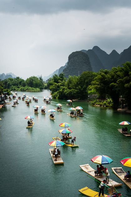Numerosas balsas de bambú con sombrillas de colores transportan turistas por un río verde entre frondosas montañas kársticas.